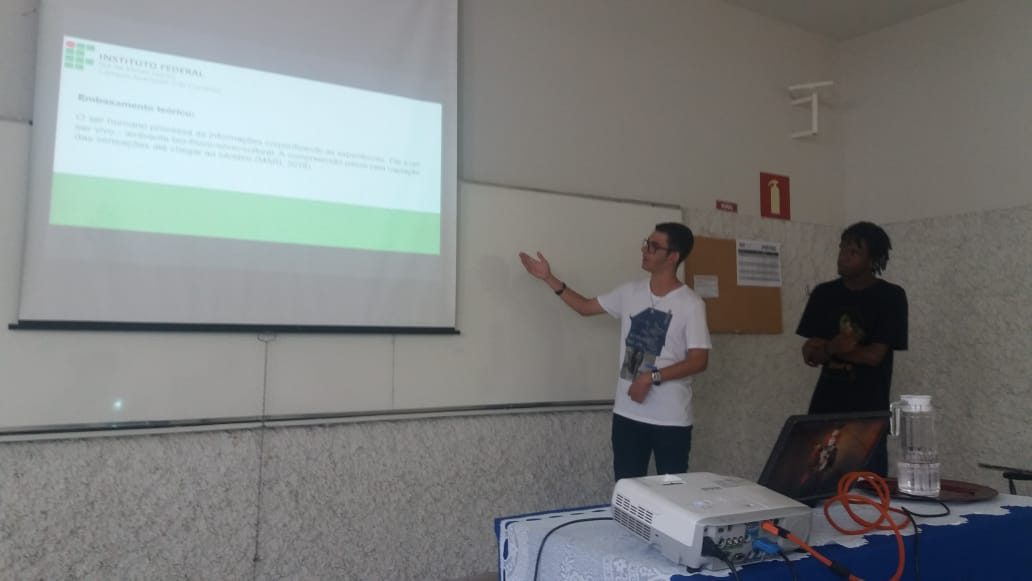 Dois alunos em sala mostram slides